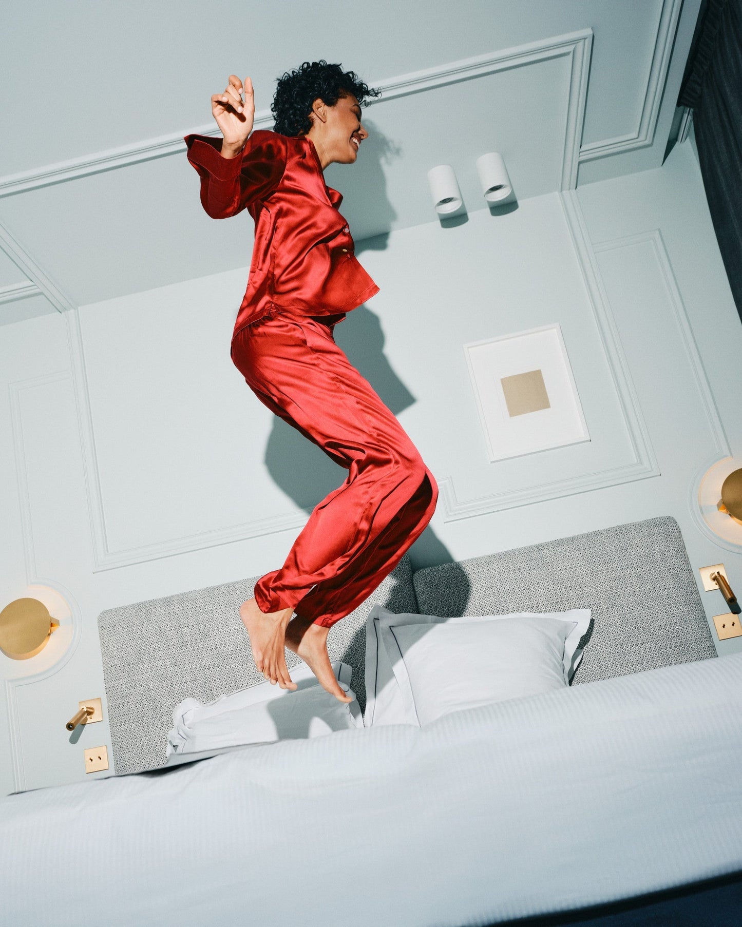black woman wearing matching silk pajama set jumping on bed