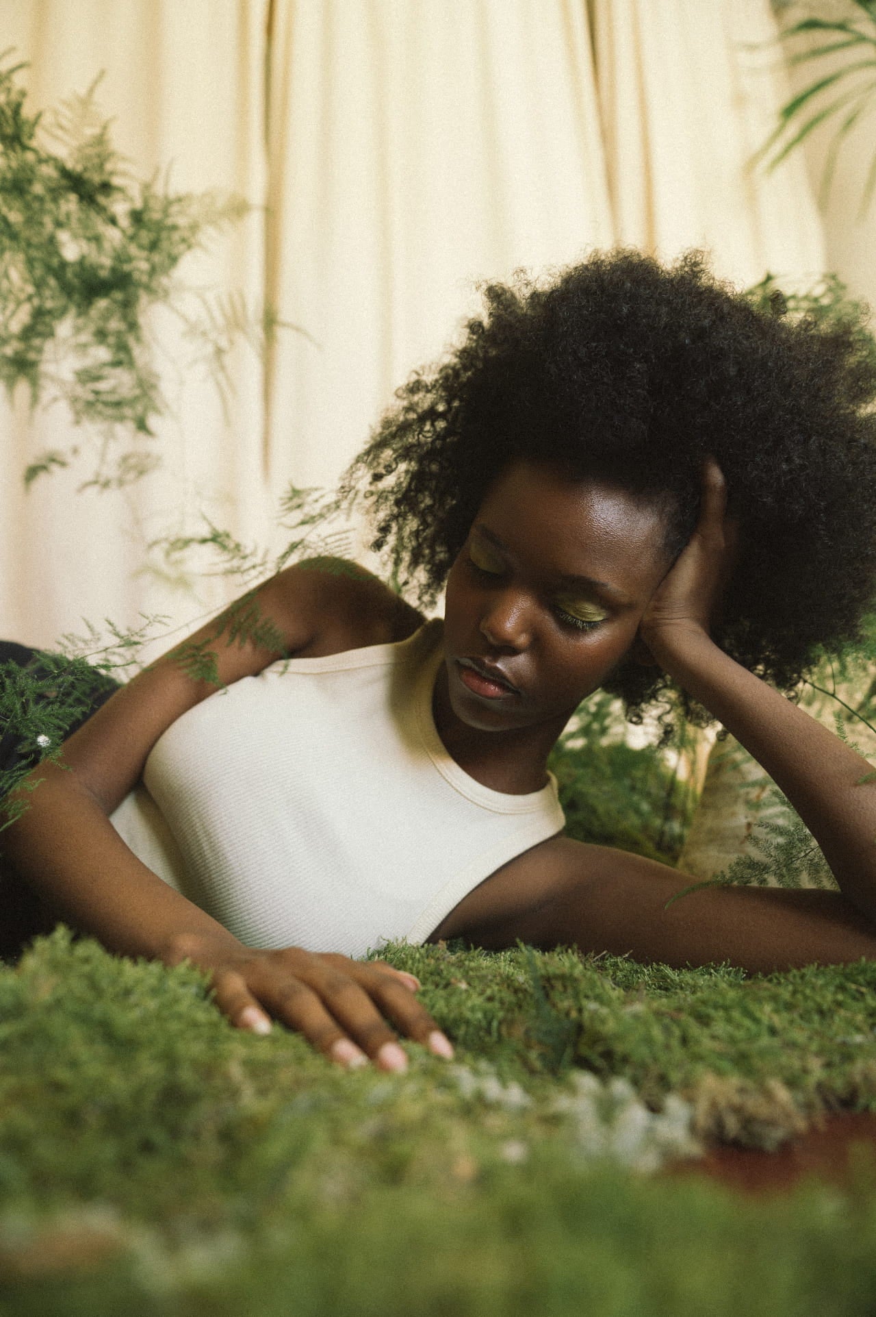 black woman with natural hair wearing white tank top lying down in the moss