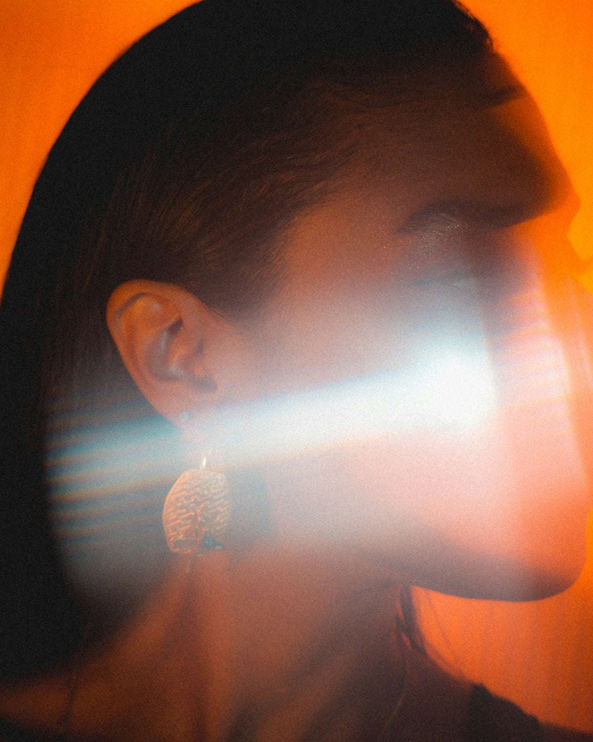 side profile of woman wearing pearl earrings on an orange background
